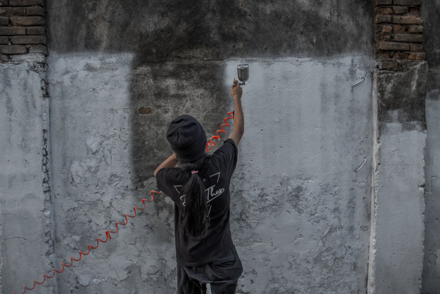 Seorang relawan yang tergabung dalam komunitas Tembok Pedia Makassar sedang mewarnai tembok yang berada di kawasan Jl. Urip Sumiharjo, Kota Makassar. Foto: Jumadil Awal