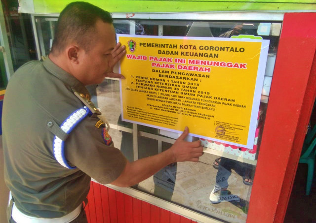 Seorang petugas Satuan Polisi Pamong Praja (Satpol PP) Kota Gorontalo, menempel stiker di rumah makan yang menunggak pajak. Kamis, (12/12) Foto : Dok Banthayo.id (Rahmat Ali)