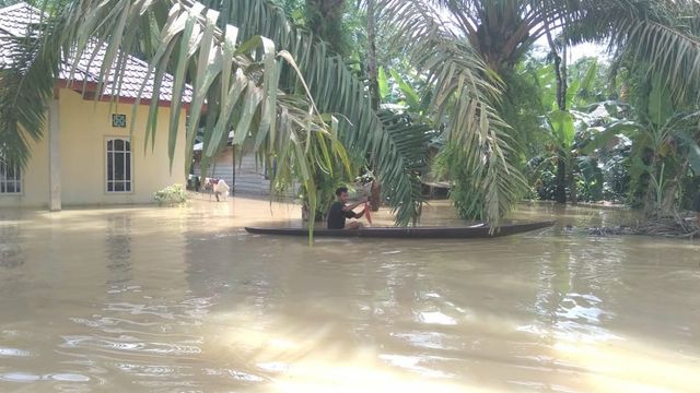 WARGA mendayung sampan di depan rumahnya yang terendam banjir akibat luapan Batang Kuantan di Kabupaten Kuantan Singingi (Kuansing). (Foto: ROBI SUSANTO)