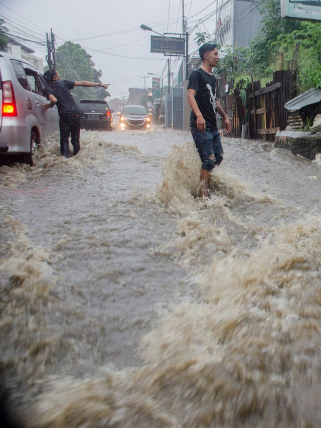 Warga membantu pengendara untuk melintasi derasnya arus air saat banjir di kawasan Cikutra, Bandung, Jawa Barat, Jumat (27/12/2019). Foto: ANTARA FOTO/Raisan Al Farisi