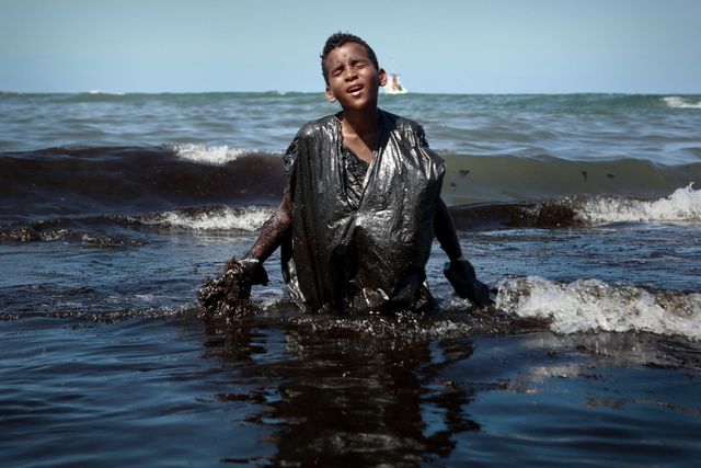 Seorang anak laki-laki keluar dari laut sambil mengeluarkan minyak yang tumpah di pantai Itapuama di kota Cabo de Santo Agostinho Brasil, pada 21 Oktober 2019.  Foto: AFP/ LEO MALAFAIA