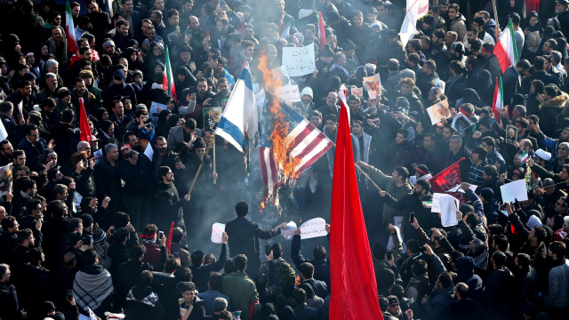 Warga Iran membakar bendera Amerika Serikat dan Israel saat menghadiri prosesi pemakaman jenazah Jenderal Qassem Soleimani di Teheran, Iran. Foto: Nazanin Tabatabaee / WANA/ via REUTERS