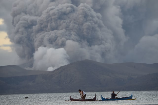 Warga menangkap ikan saat Gunung berapi Taal mengeluarkan abu vulkanik di Kota Tanauan, Filipina. Foto: AFP/Ted ALJIBE