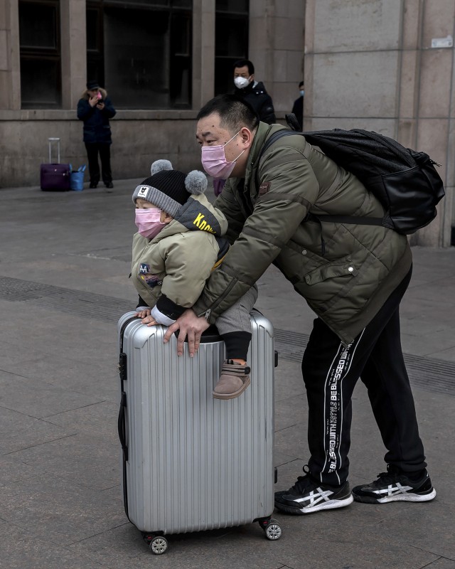 Seorang pria mendorong seorang anak yang duduk di atas koper saat mereka mengenakan masker untuk melindungi dari virus corona. Foto: Nicolas Asfouri / AFP