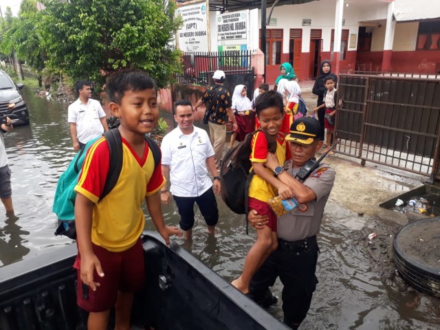 Kapolsek Medan Timur Kompol M Arifin mengevakuasi siswa SD yang terjebak banjit. Foto: Istimewa