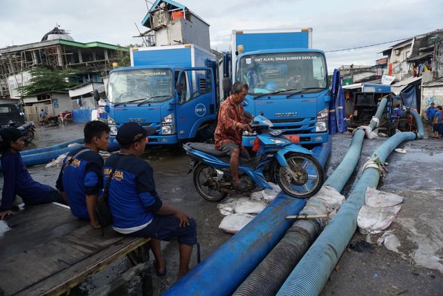 Pengendara motor melewati selang pompa yang dipasang di permukiman Jalan Dermaga Ujung, Penjaringan, Jakarta Utara. Foto: Jamal Ramadhan/kumparan