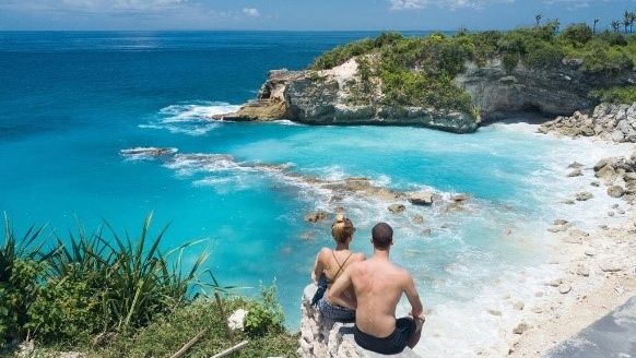 Sepasang wisatawan asing tengah menikmati lanskap laut dan pantai Bali dari atas tebing Foto: Dok. Booking.com