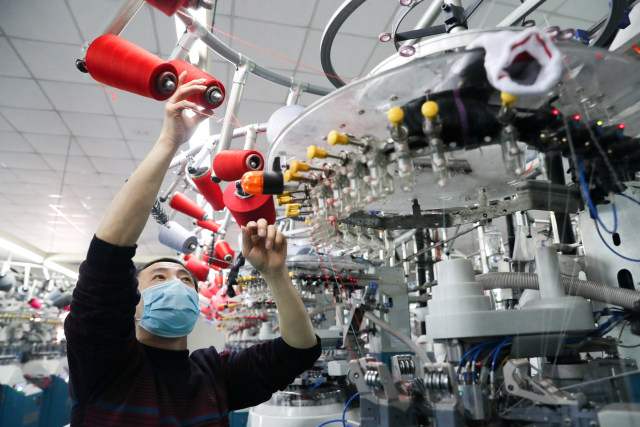 Seorang pekerja menggunakan masker menyelesaikan produksi kaus kaki di pabrik daerah Deqing Huzhou, Zhejiang, China. Foto: China Daily / via REUTERS