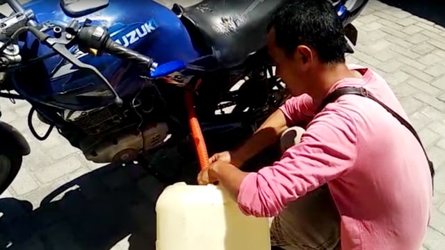 Seorang pengedara mengambil BBM dari tangki sepeda motor yang telah dimodifikasi (Foto: irwanda/Langkan.id)