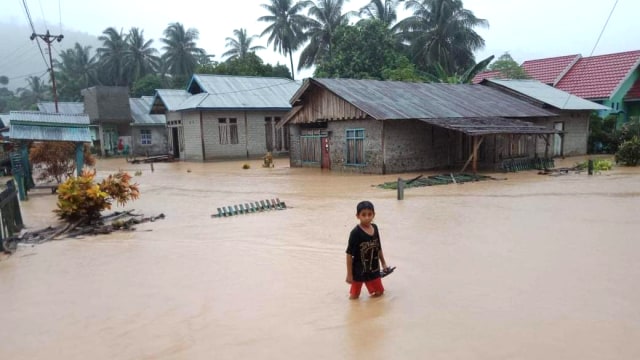 Seorang bocah saat melewati genangan air setinggi 20 cm akibat intensitas hujan yang begitu lebat di Kabupaten Tolitoli, Sulteng, pada Selasa pagi (25/2). Foto: Istimewa