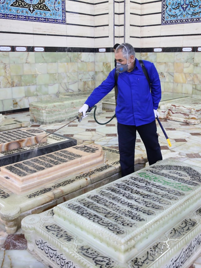 Seorang pekerja mendisinfeksi situs suci Masumeh Qom untuk mencegah penyebaran virus corona di Iran. Foto: AFP/FARS NEWS AGENCY/MEHDI MARIZAD