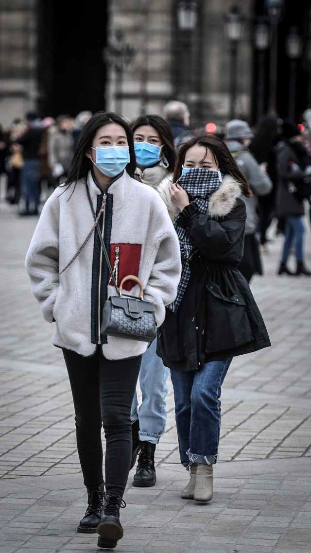 Turis mengenakan masker pelindung di tengah kekhawatiran penyebaran coronavirus novel COVID-19 di kawasan Pyramide du louvre di Paris. Foto: STEPHANE DE SAKUTIN / AFP