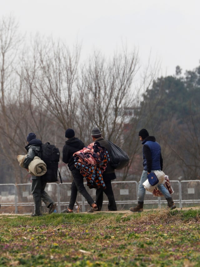 Para migran berjalan membawa barang-barang miliknya di dekat gas mata air di perbatasan Turki dan Yunani di Edirne, Turki. Foto: REUTERS / Leonhard Foeger