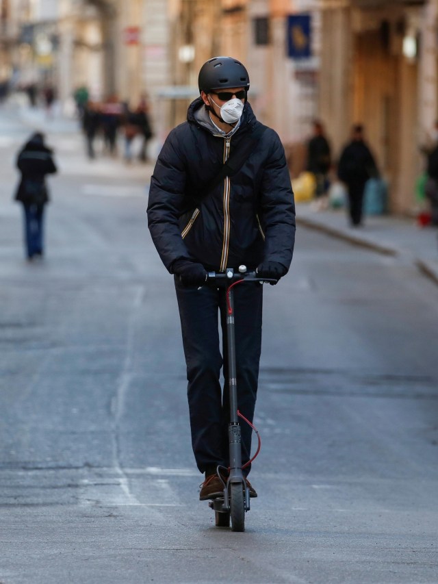 Pengendara skuter listrik melintasi jalanan yang sepi di Italia. Foto: REUTERS/Remo Casilli