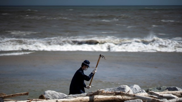 Polisi membersihkan pantai dan mencari sisa-sisa orang yang hilang setelah gempa bumi dan tsunami 9 tahun lalu di Namie, prefektur Fukusima, Jepang. Foto: REUTERS/Athit Prawongmetha