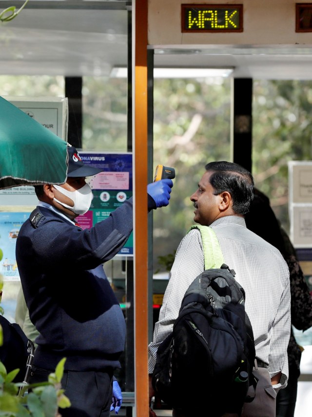 Kabar Corona Dunia - Petugas memeriksa suhu tubuh pegawai di pintu masuk gedung perkantoran di New Delhi, India. Foto: REUTERS/Adnan Abidi