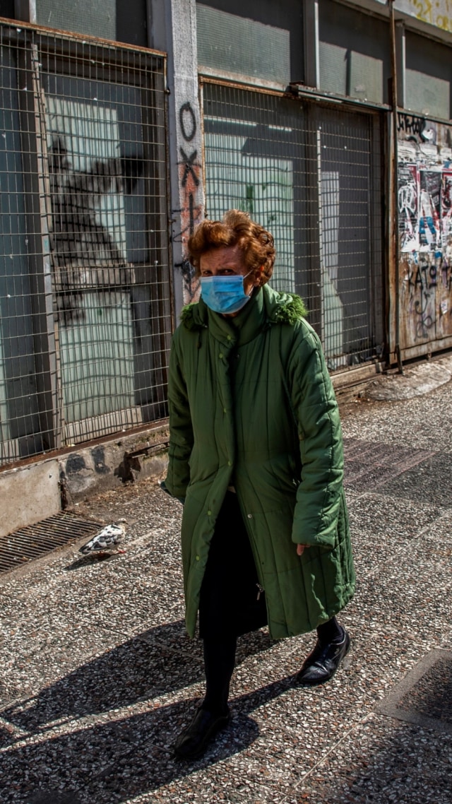 Seorang wanita mengenakan masker saat melintas di pusat Athena, Yunani. Foto: AFP/ANGELOS TZORTZINIS