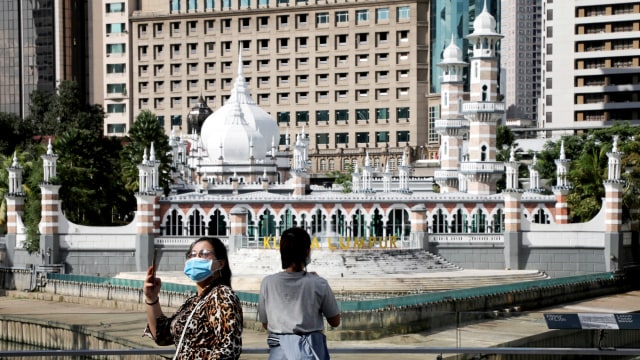 Sejumlah turis mengenakan masker berjalan di depan masjid di Kuala Lumpur, Malaysia, Senin (16/3). Foto: REUTERS/Lim Huey Teng