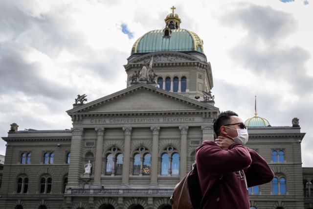 Seorang wisatawan mengenakan masker di depan Gedung Parlemen Swiss, Jumat (13/3). Foto: Fabrice COFFRINI / AFP