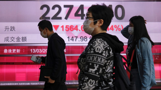 Warga menggunakan masker berjalan melewati papan informasi Indek Hang Seng di Hong Kong. Foto: REUTERS / Tyrone Siu