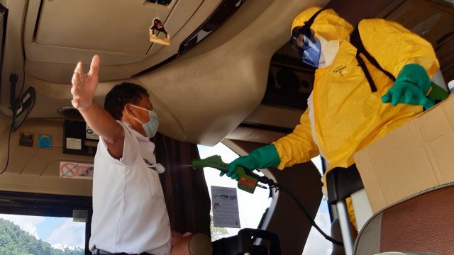 Seorang petugas Kantor Kesehatan Pelabuhan (KKP) Entikong menyemprotkan disinfektan di dalam bus Damri antarnegara dari Brunei Darussalam. Foto: ANTARA FOTO/Agus Alfian