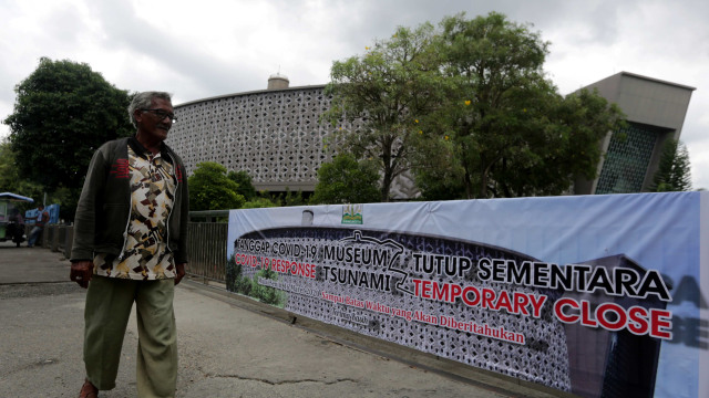 Warga melintas di depan pintu gerbang utama museum tsunami yang ditutup sementara di Banda Aceh, Aceh, Selasa (17/3). Foto: ANTARA FOTO/Irwansyah Putra