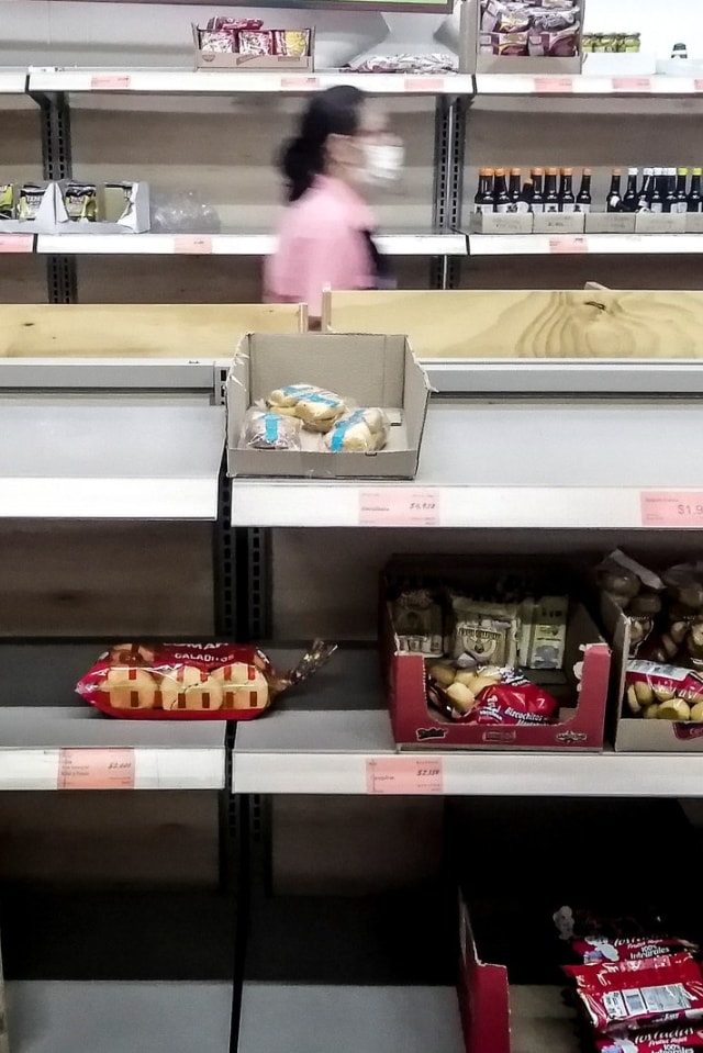 Pekerja melintasi rak makanan yang hampir kosong di supermarket Medellin, Kolombia, Selasa (17/3). Foto: JOAQUIN SARMIENTO / AFP