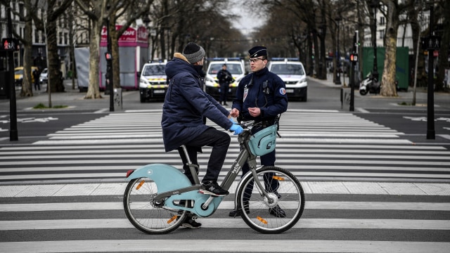 Polisi memeriksa dokumen pengendara sepeda di Place de la Bastille yang sepi saat lockdown di Paris, Prancis. Foto: AFP/Christophe ARCHAMBAULT
