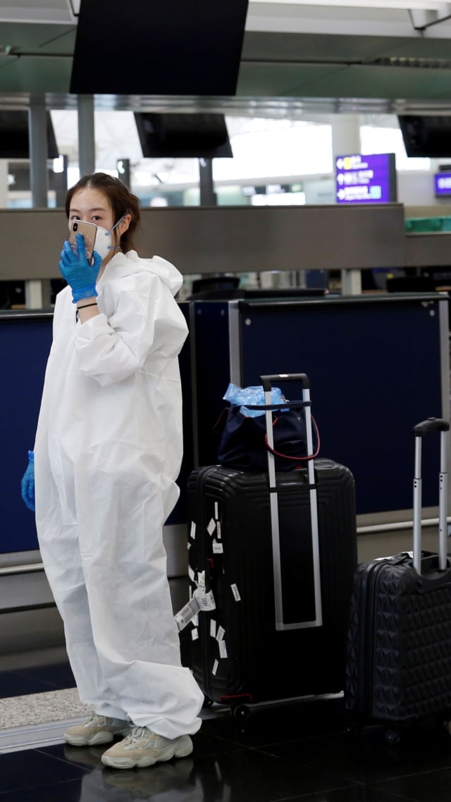 Seorang penumpang menggunakan pakaian pelindung dari plastik di Bandara Internasional Hong Kong, Hong Kong, Selasa (17/3). Foto: REUTERS/Tyrone Siu