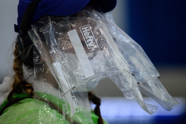 Seorang penumpang menutupi wajahnya dengan kantong plastik bekas makanan di Bandara Internasional Hong Kong, Hong Kong, Kamis (19/3). Foto: ANTHONY WALLACE / AFP