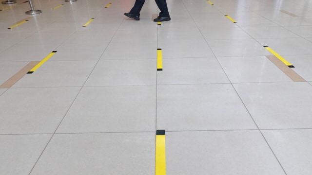 Karyawan PT Angkasa Pura II (Persero) melintas di lantai yang telah diberi stiker panduan jarak, di Bandara Depati Amir, Kota Pangkalpinang, Kepulauan Bangka. Foto: ANTARA FOTO/Anindira Kintara