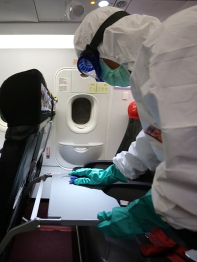 Petugas membersihkan area meja penumpang pada pesawat Airbus A320 dengan cairan desinfektan. Foto: Dok. Air Asia