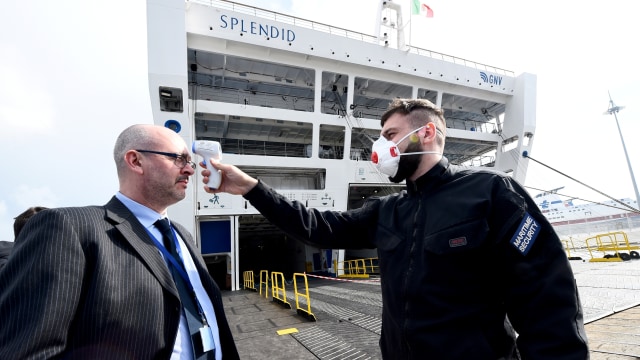 Petugas memeriksa suhu tubuh seorang pria di depan kapal pesiar Splendid yang akan digunakan untuk rumah sakit sementara pasien virus corona di Genoa, Italia. Foto: REUTERS / Massimo Pinca
