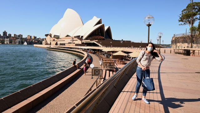 Turis menggunakan masker foto dengan latar Circular Quay di Sydney, Australia. Foto: AFP/PETER PARKS