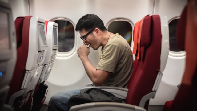 Ilustrasi penumpang pria batuk saat di pesawat. Foto: Shutterstock