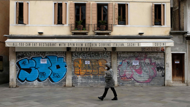 Warga Italia berjalan sambil menggunakan masker di tengah ancaman virus corona. Foto: REUTERS/Manuel Silvestri