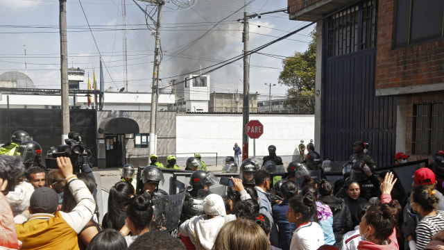 Kerabat narapidana, jurnalis dan polisi anti huru-hara berkumpul di luar ketika asap terlihat dari penjara Modelo di Bogota selama kerusuhan (22/3/2020) Foto: AFP/DANIEL MUNOZ
