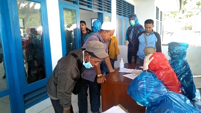 Petugas kesehatan memakai jas hujan, saat mendata penumpang yang di Pelabuhan Gita, Kota Tidore Kepulauan, Maluku Utara, untuk mencegah wabah Virus Corona. Foto: Bur