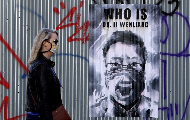 Seorang wanita mengenakan masker melewati poster almarhum Li Wenliang, seorang dokter mata China yang meninggal karena virus corona di Praha, Republik Ceko, Foto: REUTERS / David W Cerny