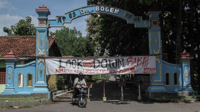 Warga melintas di depan spanduk penutupan jalan masuk Desa Bogem, Kalasan, Sleman, Yogyakarta, Senin (30/3).  Foto: ANTARA/Hendra Nurdiyansyah