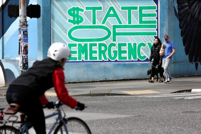 Warga melintasi mural yang bertuliskan "state of emergency" di lingkungan Capitol Hill Seattle, Amerika Serikat (29/3). Foto: REUTERS/Jason Redmond