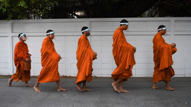 Biksu Budha menggunakan pelindung wajah saat mengumpulkan sumbangan di Kota Bangkok Thailand, Selasa (31/3). Foto: REUTERS/Chalinee Thirasupa