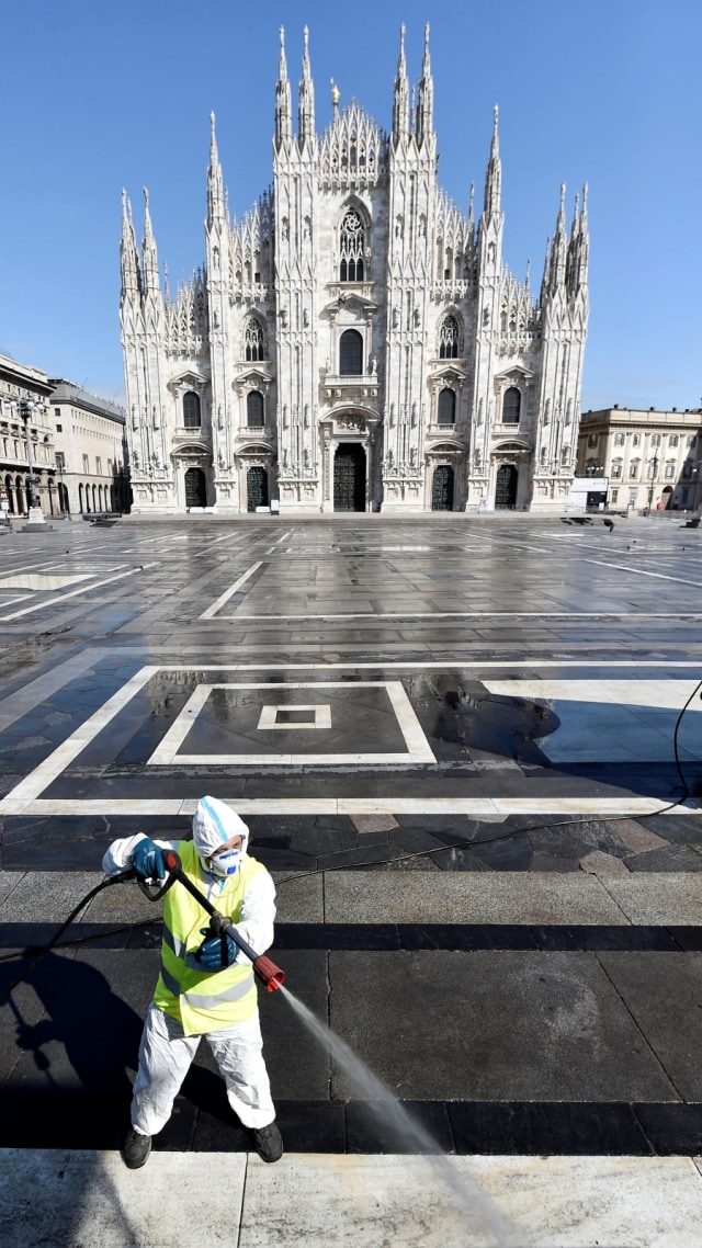 Seorang pekerja yang menggunakan pakaian pelindung menyemprotkan diisnfektan di alun-alun kota Milan, Italia, Selasa (31/3). Foto: REUTERS/Flavio Lo Scalzo
