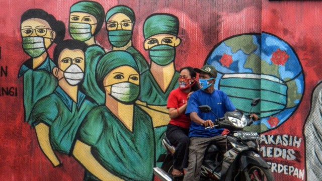 Pengendara motor melintas di depan mural tentang pandemi virus corona atau COVID-19 di Jalan Raya Jakarta-Bogor, Depok, Jawa Barat. Foto: ANTARA FOTO/Yulius Satria Wijaya
