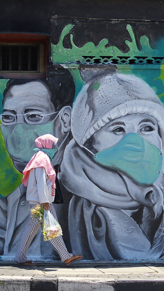 Warga melintas di depan mural Lawan Corona di Jalan Wonokromo, Surabaya, Jawa Timur. Foto: ANTARA FOTO/Moch Asim