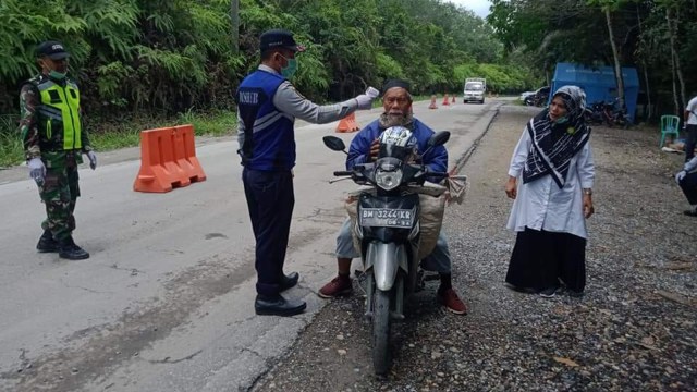 PETUGAS mengecek seorang pengendara dengan thermogun sebelum memasuki Riau dari Sumatera Barat di Pos Jaga Kuantan Singingi, Rabu, 8 April 2020. 