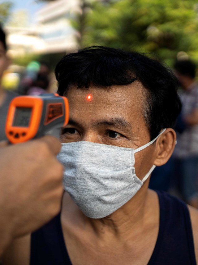 Biksu Budha dari kuil Wat Pho Nimit mengecek suhu tubuh warga saat membagikan makanan gratis kepada di Bangkok, Thailand. Foto: REUTERS/Athit Perawongmetha