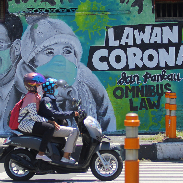 Pengendara motor melintas di depan mural Lawan Corona di Jalan Wonokromo, Surabaya, Jawa Timur. Foto: ANTARA FOTO/Moch Asim