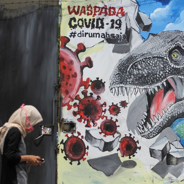 Seorang warga melintas di depan mural bertema corona di Depok, Jawa Barat. Foto: ANTARA/Asprilla Dwi Adha