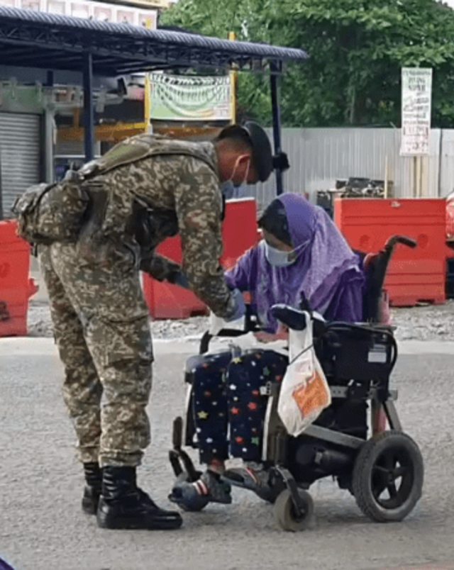 Seorang tentara di Malaysia pakaikan masker dan sarung tangan ke perempuan difabel di tengah wabah virus corona. (Foto: Facebook/Khaerul Zulkefli)